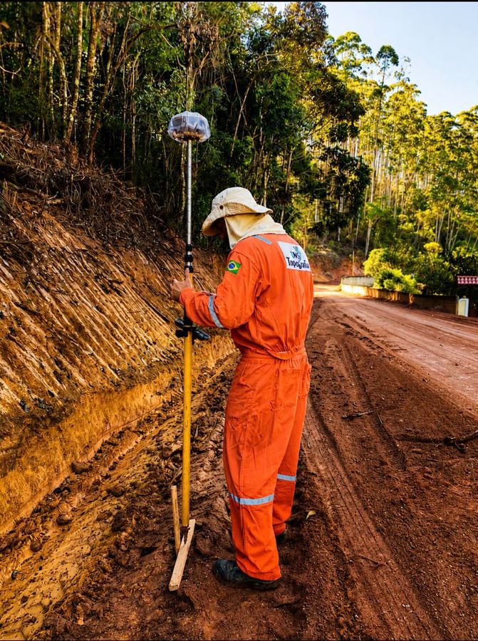 Técnico com uniforme da DMS e receptor GNSS em estrada de terra